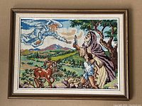 Framed embroidery of an angel reaching towards an elderly man holding a candle, with a child and goats in pastoral setting.