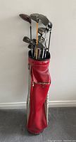 View of the full set of vintage golf clubs including irons, woods, drivers, and putter inside a red Mizuno golf bag.