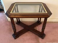 Front angle of the vintage wood glass top coffee table showing the thick glass inset with brass metal rim and turned double-spun legs with X-shaped base support.
