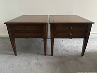 Front view of both walnut Deilcraft nightstands side by side on carpet, showing drawer fronts and handles.