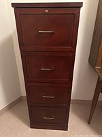 Front view of wood filing cabinet showing four drawers with metal handles, lock not engaged and no key visible.