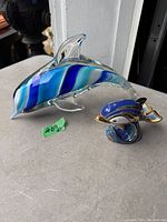 Photo showing both dolphin figurines together from the side, highlighting the larger clear blue swirled glass dolphin and smaller decorated dolphin.
