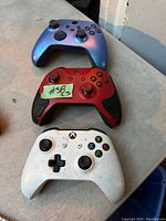 Top view of three Xbox controllers on a table, showing white, red, and blue colors.