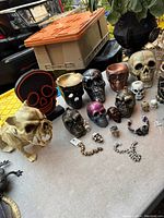 Overview of lot items on tabletop including large dog skull figurine, black neon skull light, various skull figurines, and skull bead jewelry.