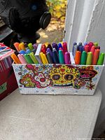 Decorative box with multiple multi-colored Sharpie marker pens showing colorful Day of the Dead design on the box