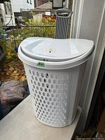 Front angled view of white plastic clothes hamper with lid closed and ventilation holes visible