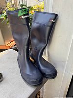 Front and side view of the pair of tall black rubber boots with Baffin logo on the shaft.