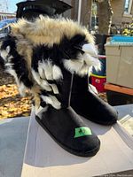 Front angle photo showing black fuzzy boots with thick fur trim in cream, black, and white hues. Label with size 9 visible.