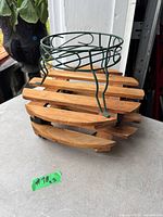 Photo showing a round wooden rolling plant stand with caster wheels, topped with a green metal wire pot holder with three legs