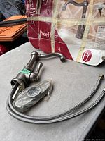 New Price Pfister kitchen faucet in bronze finish, single handle lever, braided supply lines, original packaging shown in rough condition and discarded.