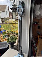 Full length view of the Shark Rocket stick vacuum standing upright on a table against a pillar outside, showing lightweight stick design and power switch.