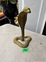 Solid brass cobra statue with raised hood and coiled body on a table surface, showing detailed scale texture and brass finish.