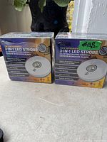 Photo shows two boxed Kidde 3-in-1 LED strobe smoke and carbon monoxide alarms. The boxes are white and purple with product images and feature highlights.