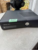 Front and top view of black Xbox 360 console showing disc drive with Xbox 360 branding and ventilation grills.