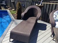 View of brown resin wicker chaise lounge placed on a deck next to a pool, showing its curved backrest and ergonomic seating design.