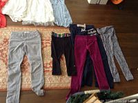 Multiple girls clothing items including pants and dresses arranged on floor showing variety of styles and colors