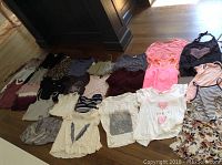 Spread of approximately 20 small girls tops and tank tops in various colors including pink, white, black, gray, with stripes and floral patterns.