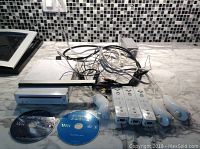 Top-down view of all bundle components including the Wii console, sensor bar, power and AV cables, four Wii remote controllers with wrist straps, and two game discs labeled 'Crash' and 'Play that one!'