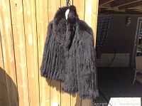 Front view of medium blue fox fur coat hanging on wooden fence