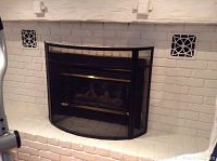 Curved black metal fireplace cover installed on white brick fireplace with visible gold-tone horizontal accents.