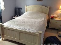 Full view of cream-colored solid wooden bed frame with vertical panel design on headboard and footboard, bed made with light bedding.