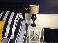 White wooden side table with lamp placed beside bed with striped bedding