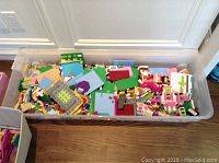 Large plastic box filled with assorted Lego pieces scattered inside.