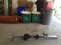 Photo showing full length of two silver and black Head skis with bindings stacked together on the floor.