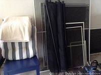 Photo shows two striped cushions on a blue chair in front of several window screens and two rolled black mesh safety fence panels with poles leaning against the wall.