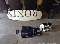 Full view of Ronix wakeboard, white wakeboard boots, black O'Neill vest, and two fins on concrete floor