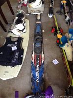Photo showing one O'Brien water ski, two pairs of water skis with attached bindings and life jackets on the floor.