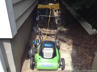Green and black Craftsman electric lawnmower with yellow extension cord coiled around handle, parked outside next to a house siding.