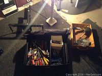 Black toolbox on floor containing assorted hand tools and hardware; TV wall mount bracket is behind the toolbox.