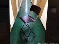 Side view of one foldable bar stool showing wooden seat and backrest on metal frame with footrest.