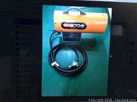 Photo of Dynaglo Pro propane heater with hose and regulator coiled underneath on green surface.