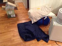 Photo showing a partially unrolled blue sleeping bag next to folded bedding items on wood flooring.