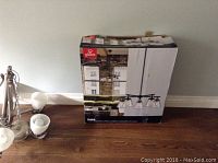 Photo shows the boxed pendant light fixture and some of the unassembled components including the glass shades and metal parts on the floor next to the box.