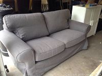 Front view of IKEA grey fabric loveseat sofa with two cushions, rounded armrests and skirted base.