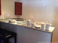 Wide view of glassware and dishes on kitchen counter, showing all items included in the lot.
