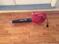 Side view of the red Homelite electric leaf blower with attached black nozzle on a wooden floor.