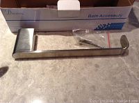 Heavy stainless steel towel bar with mounting hardware on countertop, slightly reflective surface.