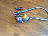 Front view of Dyson Ball vacuum body on wood floor, flexible hose and detached wand with small attachment