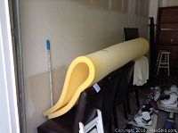 Yellow foam mattress topper folded in a wavy shape, placed over chairs inside a room.
