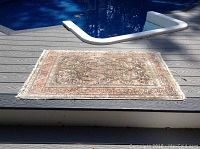 Carpet laid out on outdoor deck near pool, showing overall size and condition
