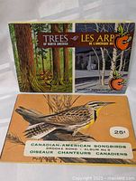 Two Brooke Bond Tea Card sets from the 1960s: "Trees of North America" album with illustrations of forest scenes, and "Canadian-American Songbirds Album No. 9" featuring a bird illustration on the cover.