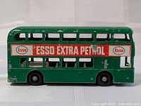 Side view of green vintage double-decker Daimler bus model with Esso Extra Petrol advertising on side showing paint chipping and wear.