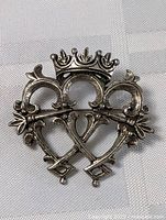 Close-up photo of antique silver brooch with three arches, crown on top, and crossed keys design.