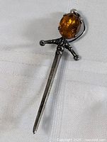 Full view of vintage sterling silver sword-shaped brooch with oval faceted citrine stone at the hilt, laid on white fabric.