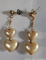Pair of vintage gold plated earrings with two pearlized cream heart-shaped charms hanging on each. Mismatched clasps visible.