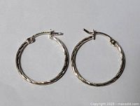 Pair of sterling silver carved hoop earrings laid flat on a white background.